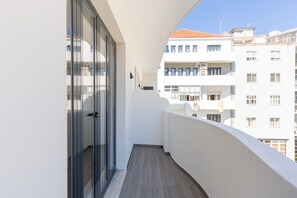 A narrow balcony with a glass door, white walls, and a view of adjacent buildings.