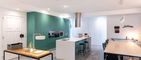 A modern kitchen with teal cabinetry, a central island, and a dining area with a long table and chairs.
