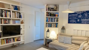 Een woonkamer met een bank, een salontafel en een televisie. Er staan boekenkasten met boeken en decoratieve objecten.