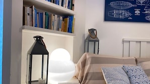 Een slaapkamer met een bed, een nachtkastje met een lantaarn, een boekenplank en een kunstwerk aan de muur.