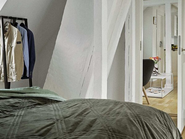A bedroom with a bed, a clothing rack, and a hallway leading to a bathroom.