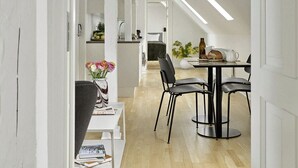 Un espace de repas moderne avec une longue table et des chaises, un vase de fleurs et une cuisine en arrière-plan.
