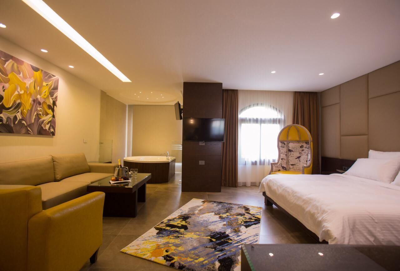 A hotel room with a sofa, a bed, a flat-screen TV, a bathroom, and a large abstract painting on the wall.