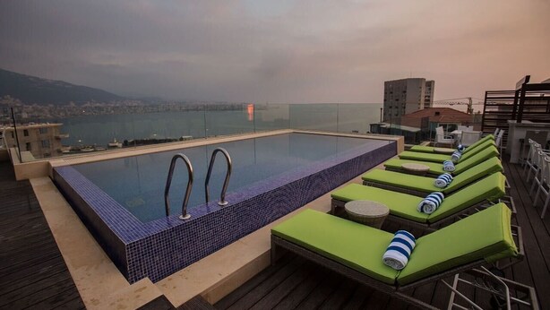 A rooftop infinity pool with a view of the city and sea, surrounded by lounge chairs and a wooden deck. - The Opera Hotel (Kfar Yassine)