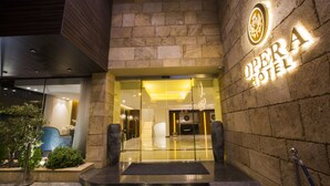The entrance of the Opera Hotel with a glass facade, a stone wall, and a sign with the hotel's name. - The Opera Hotel (Kfar Yassine)