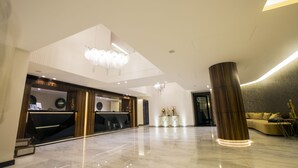A modern lobby with a reception desk, a large chandelier, and a seating area with a sofa and decorative plants. - The Opera Hotel (Kfar Yassine)