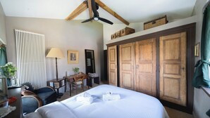 Una habitación de hotel con una cama grande, armario de madera, escritorio, silla y un ventilador de techo.