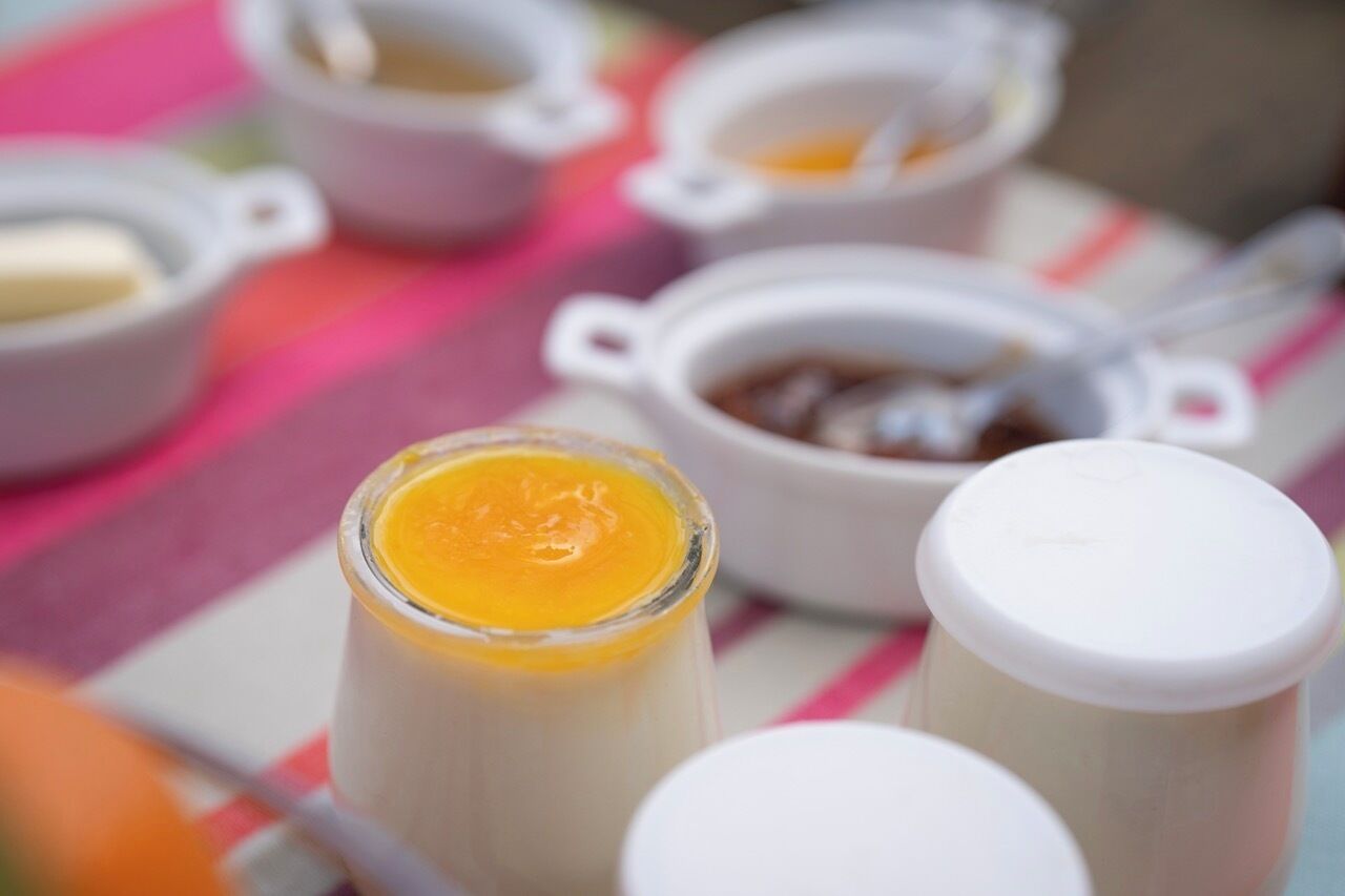 A table with various food items, including a jar of yellow sauce, small bowls with sauces, and a container with a lid.