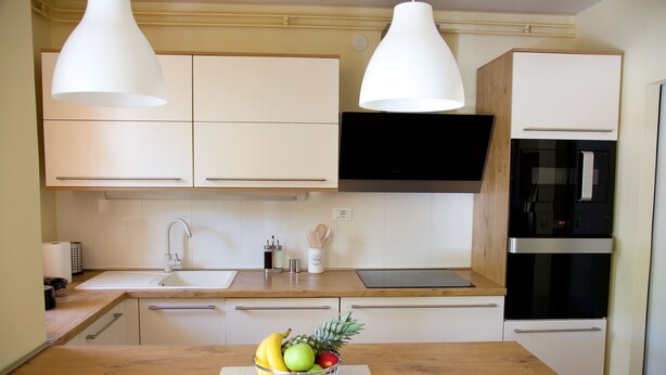 Una cocina moderna con armarios blancos, horno de acero inoxidable y un frutero en la encimera.