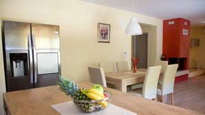 Una cocina moderna con electrodomésticos de acero inoxidable, un comedor con mesa y sillas de madera, y un frutero sobre la mesa.