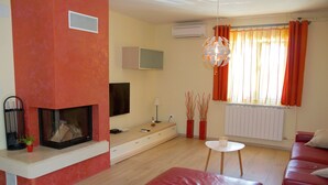 Una sala de estar con chimenea, sofá rojo y televisor montado en la pared.