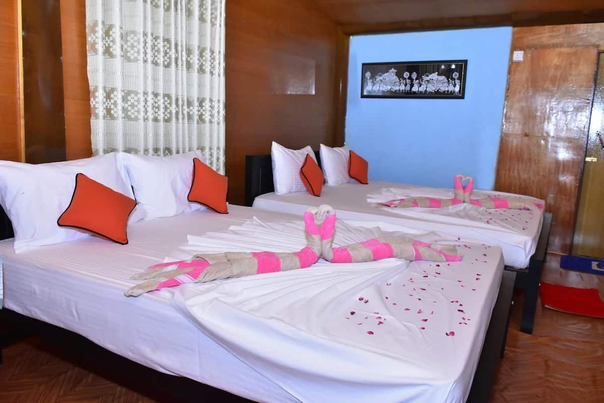 A hotel room with two beds, each with white linens and orange pillows. There is a framed picture on the wall and a wooden floor.