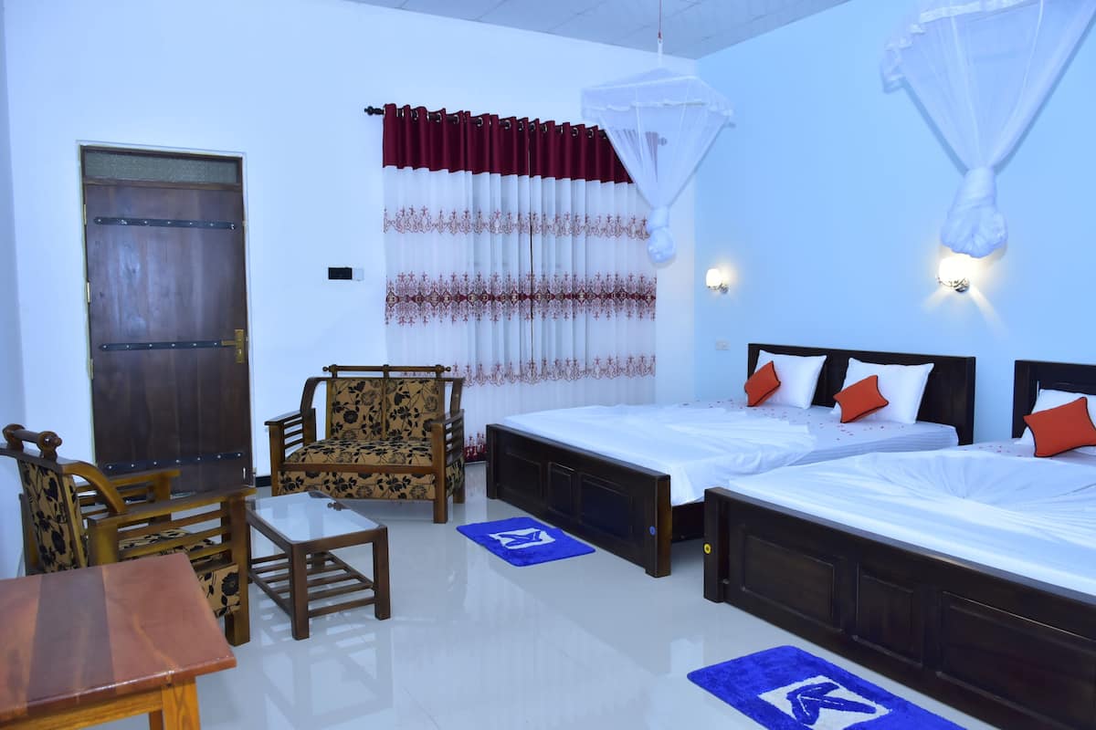 A hotel room with a wooden bed, two single beds, a wooden chair, a small table, a window with curtains, and a mosquito net.