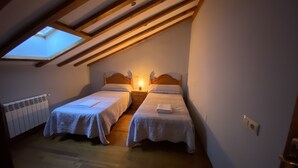 Een klein, gezellig slaapkamer op zolder met twee eenpersoonsbedden, een dakraam en een radiator.