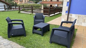 Een terras met rieten meubilair, een pad van stenen en uitzicht op omliggende gebouwen.