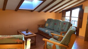 Een gezellige woonkamer met een hoge plafond, houten balken, een bank met gestreepte kussens, een houten salontafel en een raam met uitzicht.