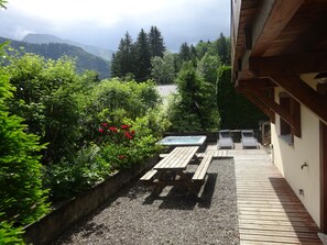Une terrasse en bois avec un jacuzzi, un espace salon et une vue sur un paysage montagneux.