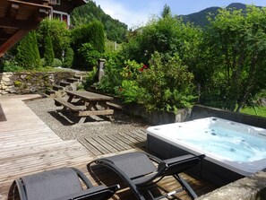 Une terrasse en bois avec un jacuzzi, des chaises longues et un mur en pierre agrémenté de plantes grimpantes.