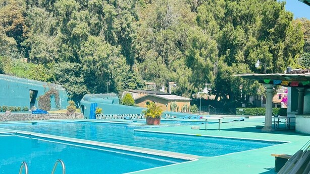 A swimming pool with a hammock, a lounge area, and a view of trees and buildings. - Club Santa Maria (Cuernavaca)