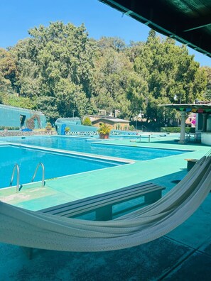 Una piscina amb un hamaca, zona de relaxació i vistes a arbres i edificis.