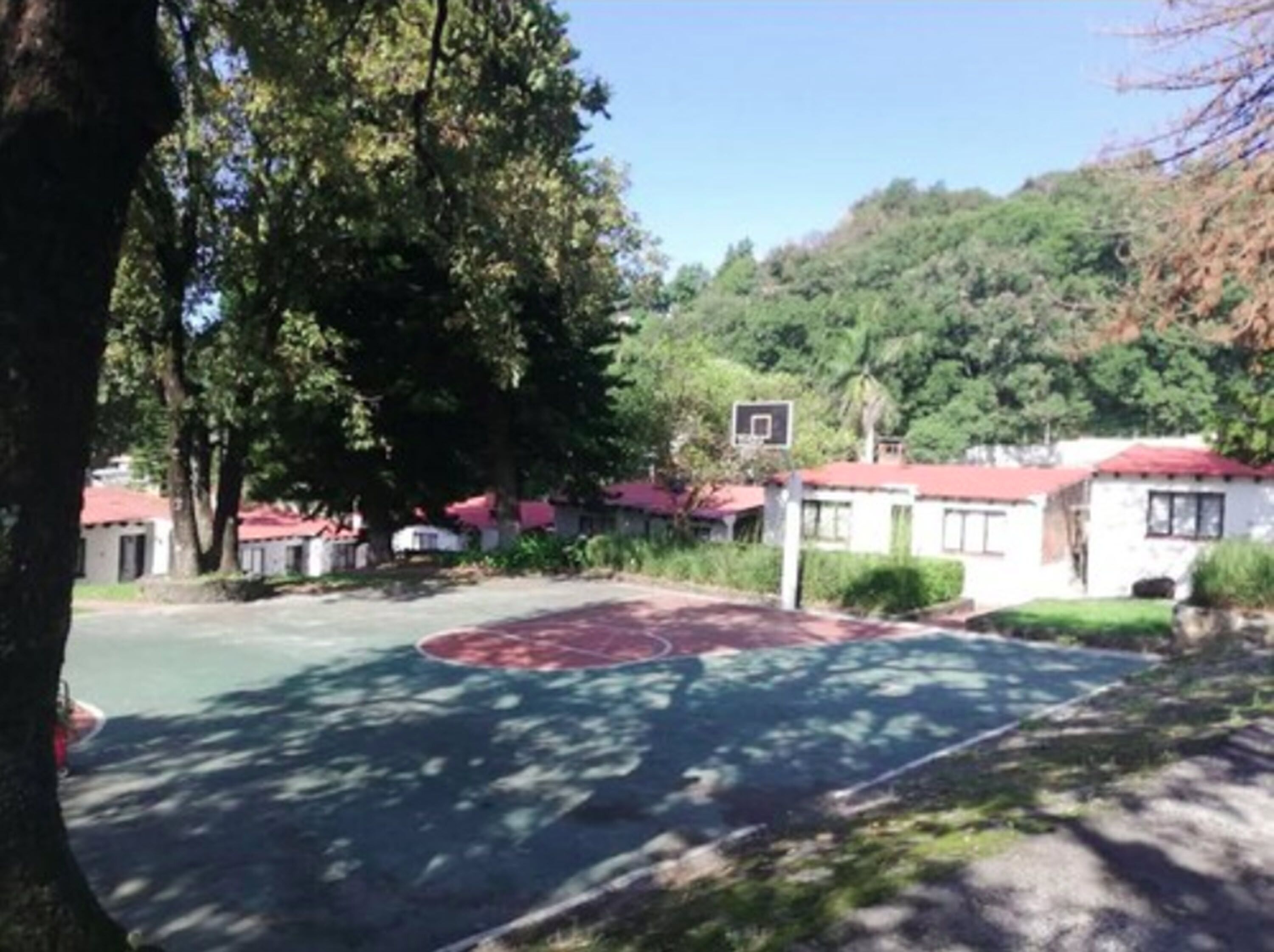 Uma quadra de basquete cercada por árvores e edifícios com telhados vermelhos.