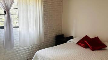 A bedroom with a bed, white curtains, a brick wall, and a tiled floor.
