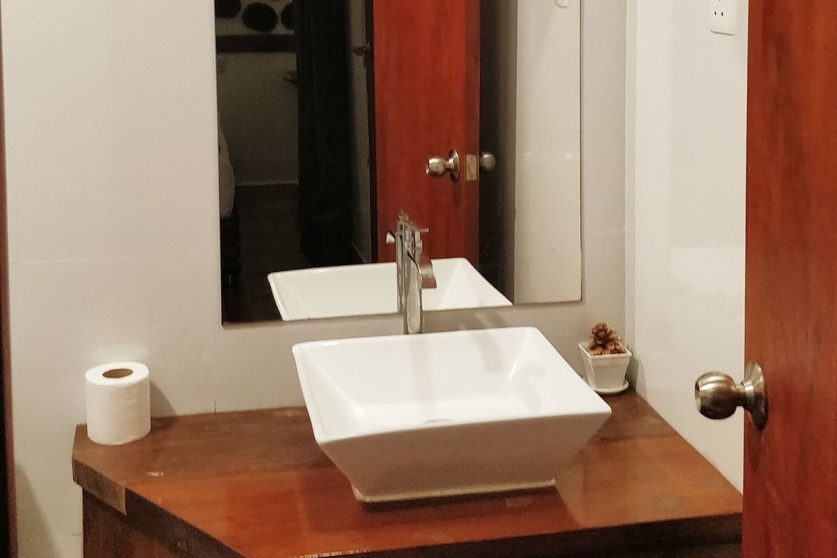 Un baño con lavamanos blanco, un espejo y tocador de madera.