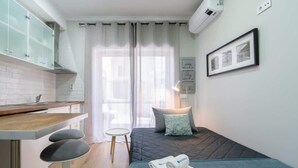 A modern hotel room with a kitchenette, a bed with a blue bedspread, a small round table, and a framed picture on the wall.