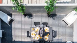 A rooftop patio with a table set for four, surrounded by chairs, and two potted plants.