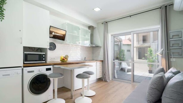 A modern kitchen with a washing machine, a microwave, and a dining area with stools.