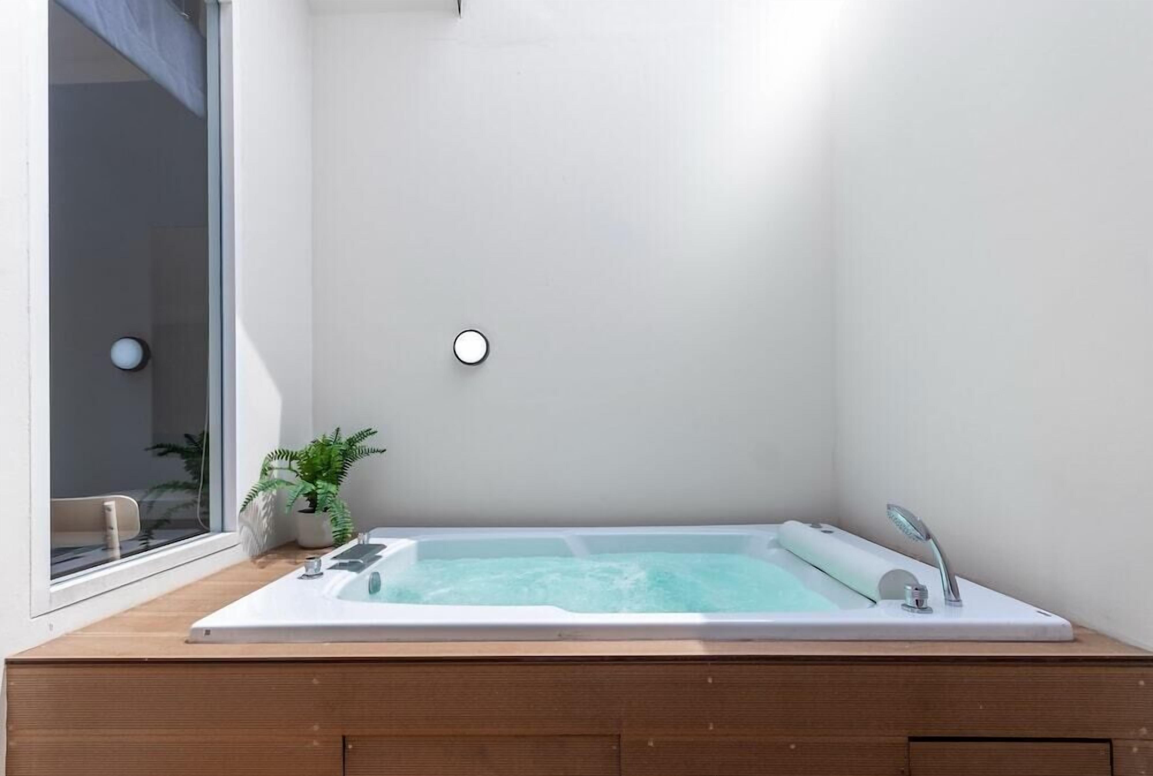 A modern bathroom with a large bathtub, a potted plant, and a window.