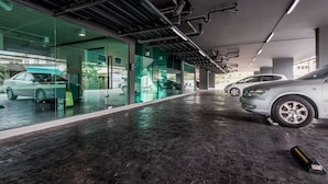 A modern indoor parking garage with glass walls, a wet floor, and cars parked inside. - Nidhra Residence (Lam Luk Ka)