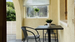 A patio with a table and chairs, a potted plant, and a window with blinds.