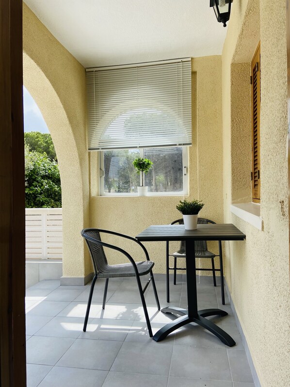 Een terras met een tafel en stoelen, een bloempot en een raam met zonwering.