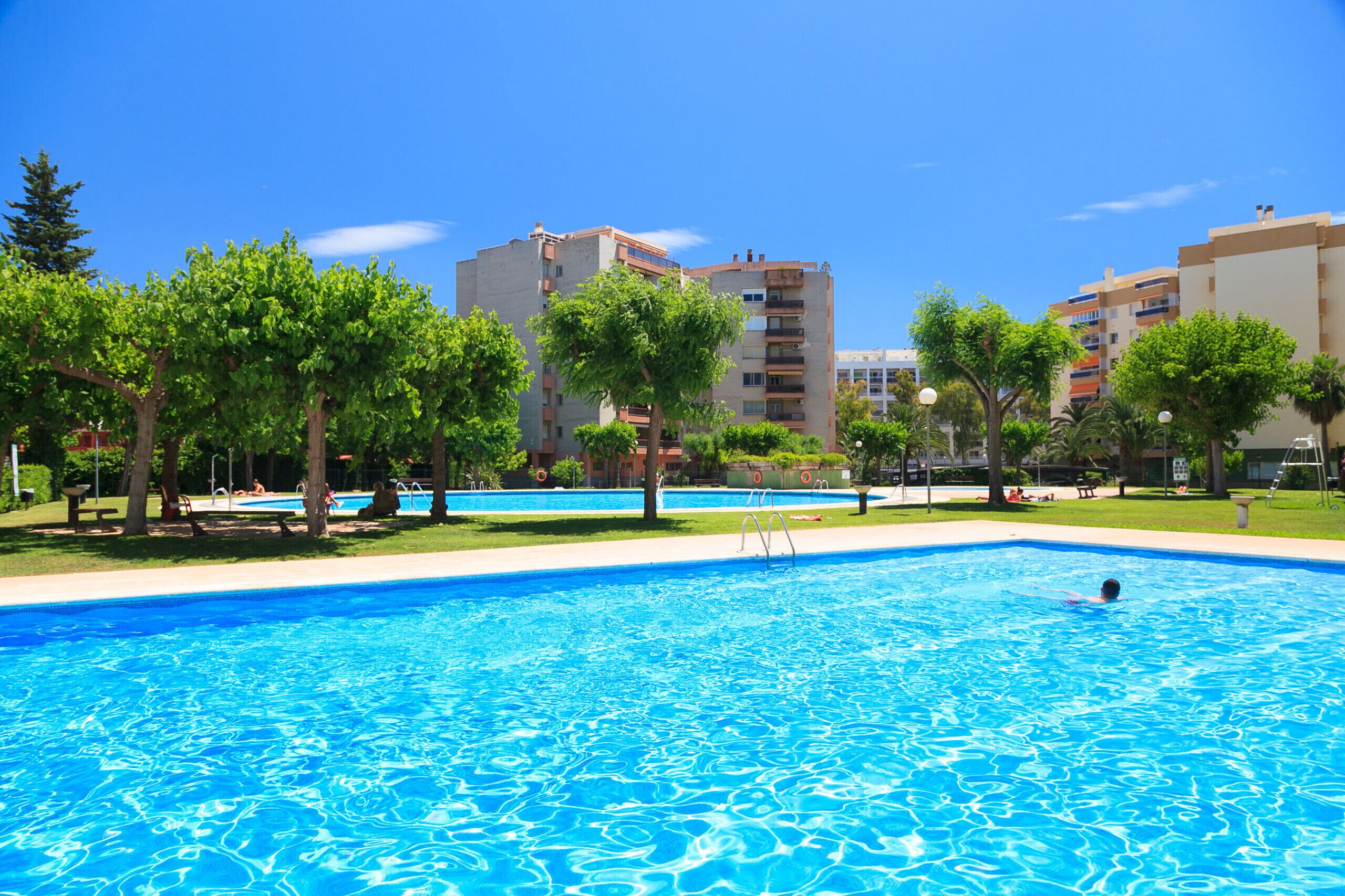 A swimming pool with clear blue water, surrounded by trees and buildings.