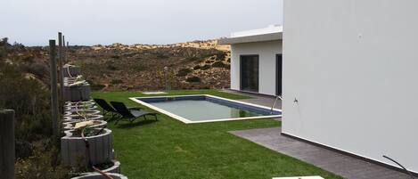 A modern outdoor pool area with a rectangular pool, surrounded by a well-maintained lawn and a stone pathway.