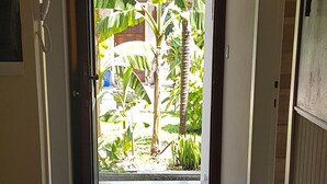 Un pasillo con felpudo que lleva a una puerta, un pequeño espacio exterior con plantas y una vista de un edificio de techo rojo.