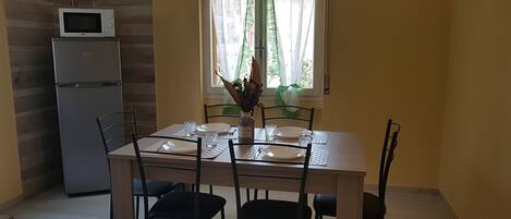 Ein Essbereich mit einem Tisch für vier Personen, einem Kühlschrank und einer Wand-Mikrowelle.