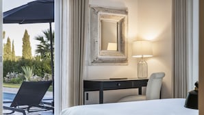 Ein Hotelzimmer mit einem Bett, einem Schreibtisch mit Lampe, einem Sessel und einem großen Spiegel.