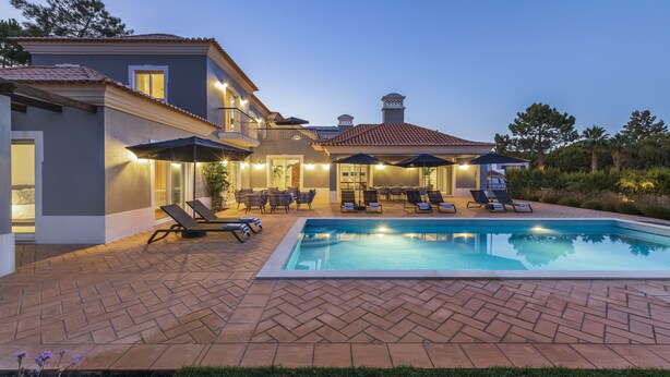 Ein zweigeschossiges Haus mit Schwimmbad, Sitzgelegenheiten im Freien und einer überdachten Terrasse.