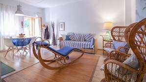 A living room with a sofa, two rocking chairs, a dining table with chairs, a lamp, and a window with curtains. - Apartment Le Cannucce at the sea of Castiglione (Castiglione della Pescaia)
