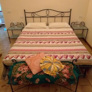 A bed with a striped bedspread, two pillows, a bedside table, and a bench with a floral cushion. - EDERA bed and breakfast (Porto Sant'Elpidio)