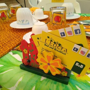 A table with breakfast items, including a can of fruit, a white teapot, and a yellow card with 'L'Edra Bed and Breakfast' branding. - EDERA bed and breakfast (Porto Sant'Elpidio)
