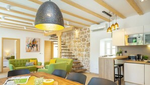 A modern kitchen with a microwave, stove, and sink. There is a dining area with a wooden table and chairs. A green sofa and a yellow table runner are also visible. - Hedera Estate, Villa Hedera IV (Dubrovnik)