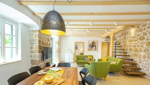 A modern living room with a stone wall, a green sofa, and a wooden dining table. - Hedera Estate, Villa Hedera IV (Dubrovnik)