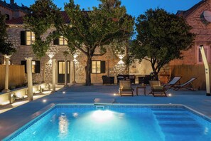 A swimming pool with lounge chairs and a stone building with outdoor lighting. - Hedera Estate, Villa Hedera IV (Dubrovnik)