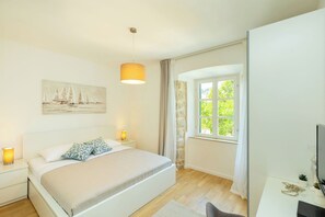 A bedroom with a bed, bedside lamps, a painting, a window, and a desk with a computer. - Hedera Estate, Villa Hedera IV (Dubrovnik)