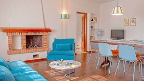 Ein modernes Wohnzimmer mit Kamin aus Backstein, blauen Sofas, einem runden Couchtisch und einem Essbereich mit Stühlen sowie einem Fernseher.