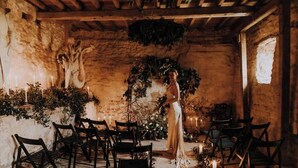 A rustic interior with stone walls, wooden beams, and a central aisle with chairs.