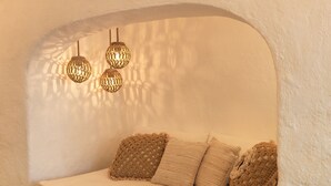 Een gezellige, gewelfde zithoek met een beklede bank, gebreide kussens en hangende geweven lampen.